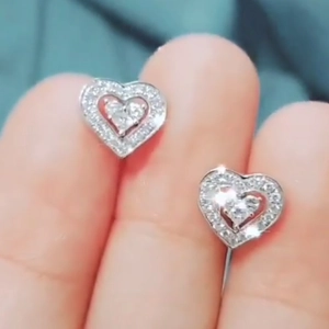 Macro shot of silver heart stud earrings with cubic zirconia on a model's earlobe