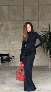 Détail des fronces à la taille sur robe noire à col montant avec sac à main rouge