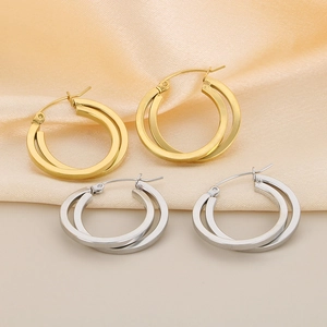 Close-up of interlocking gold and silver titanium steel hoop earrings on silk fabric