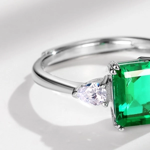 Macro shot of silver ring with princess cut emerald green stone and white pear side stones