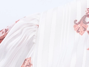 Dettaglio di abito bohémien bianco con stampa paisley rosa e spalla a pieghe tessuta