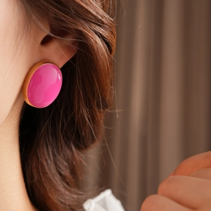 Close-up of vintage oval gold earrings with pink glaze worn by a model in soft lighting
