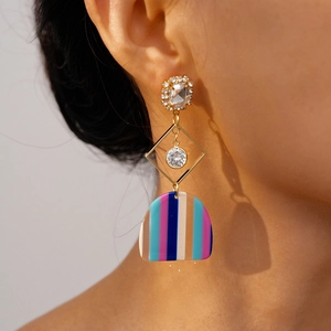 Close-up of geometric resin drop earrings with colorful stripes and gold crystal studs