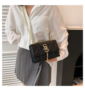 Detail of black quilted leather shoulder bag with gold S-buckle and metal tassel