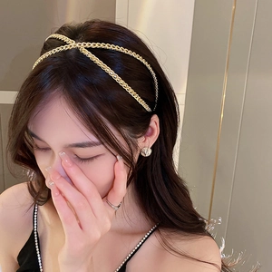 Gros plan d'un serre-tête croisé en chaîne dorée porté par une femme au style élégant