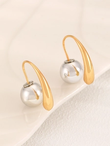 Detail view of modern mixed-metal earrings with gold teardrop hooks and silver metal spheres