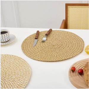 Detail of round woven placemats in gold and white on a dining table with tableware