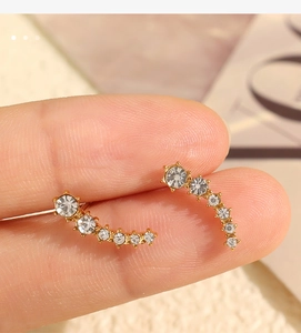 Detail view of crescent curved gold stud earrings with shimmering white crystals in hand