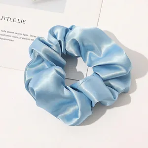 Macro detail of sky blue silk satin scrunchie showing glossy texture and pleats