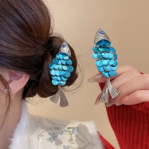 Detailed macro view of fish-shaped earrings with blue scales and silver metallic fish tail