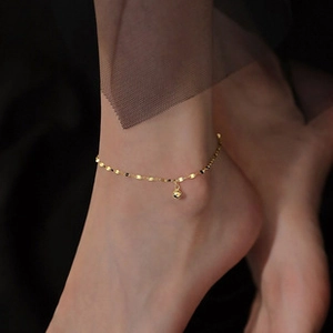 Detailed close-up of a minimalist golden anklet with small sphere pendant on dark background