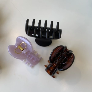 Three square hair claws in matte black, glossy purple, and amber colors on a white surface