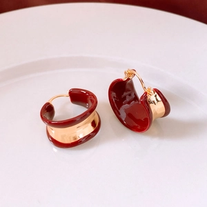 Detail of 18k gold plated C-shaped earrings with burgundy enamel on a white ceramic plate