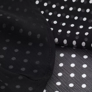 Dettaglio del tessuto in chiffon nero a pois bianchi con morbide pieghe e caduta