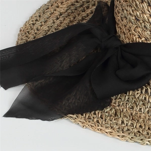 Detailed close-up of woven straw sun hat featuring a large elegant black ribbon bow