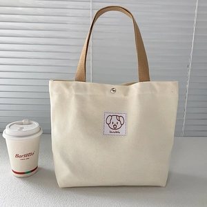 Close-up of a cream canvas tote bag featuring a cute puppy patch and brown woven handle