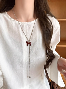 Detail of silver snake chain necklace featuring a reddish-brown pony pendant on a model
