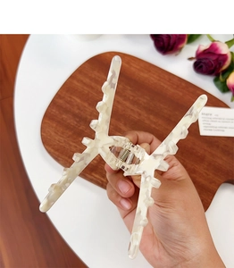 Detailed view of a cream marble pattern acetate hair claw clip on a rustic wooden table