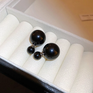 Detailed close-up of elegant black double pearl earrings in a white jewelry box