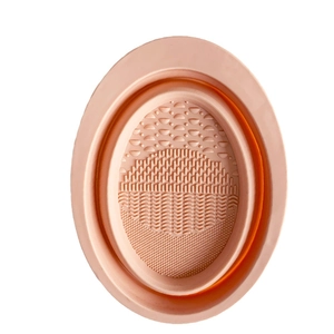 Pink silicone makeup brush cleaning mat with varied textures on white background