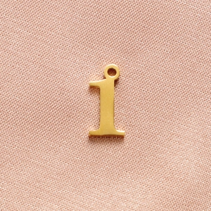 Polished gold-plated number 1 pendant detail for DIY jewelry on pink fabric background