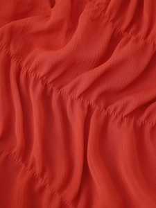 Macro detail of red ruched chiffon fabric showing fine pleated texture and stitching line
