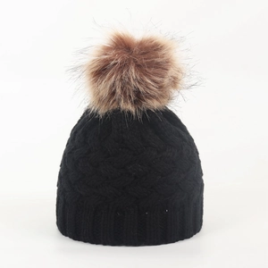 Detail of black knit baby winter hat featuring a large brown faux fur pom pom