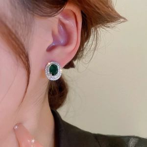 Close-up of emerald green oval zircon stud earrings with double halo stones on ears