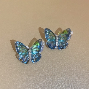 Close-up of blue butterfly stud earrings with pearls and gold foil on beige leather