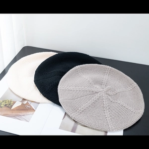 Flat lay detail showing beige, black, and grey knitted beret hats with thick yarn texture
