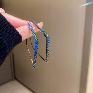 Detail of hand holding geometric hoop earrings with gradient blue rhinestones