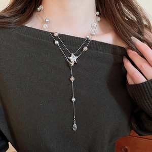 Detail of star pendant Y-shaped double layer necklace with pearls on green knitwear
