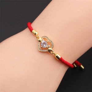 Detail of red braided bracelet with a golden heart pendant and sparkling zircon stone