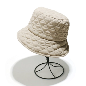 Detailed texture of beige quilted puffer bucket hat on a minimalist metal display stand