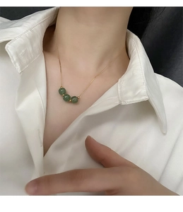 Detail of vintage gold necklace featuring three green jade beads on a titanium steel chain