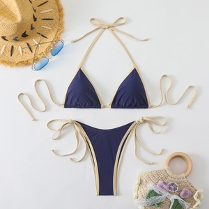 Flat lay of navy blue bikini with cream ties, sun hat and beach bag for summer vibes