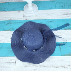 Close-up of dark blue straw sun hat with delicate white flowers and pearl embellishments