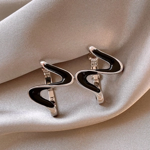 Macro view of silver wave-shaped earrings with black enamel detail on silk fabric