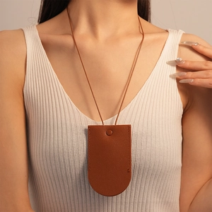 Detail of brown faux leather mini pouch necklace with metallic snap button on white top