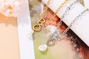 Detail of gold and silver letter B necklaces with white baroque pearls on a magazine