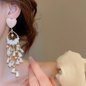 Close-up of elegant long tassel earrings with ivory heart studs and golden metal accents