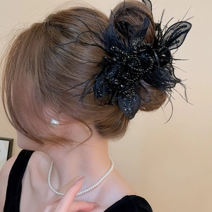 Detail of elegant black fabric hair claw with pearls, sequins and feathers on a bun
