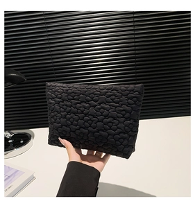 Detail of a black quilted clutch bag featuring elegant 3D floral texture and soft nylon fabric