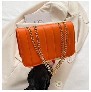 Detailed view of orange PU leather flap bag with gold chain strap on beige blazer