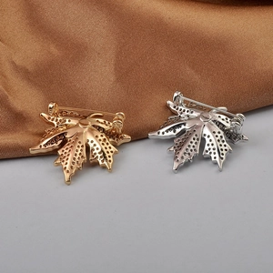 Detailed back view of gold and silver maple leaf brooches showing the pin and hollow metal