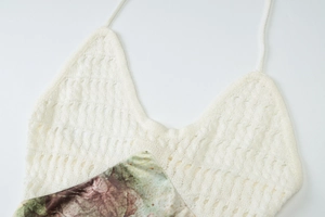 Close-up of white hollow knit lace bodice stitched with green floral print fabric