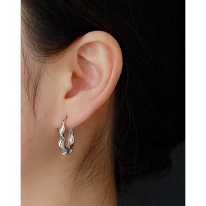 Close-up of minimalist silver irregular wavy hoop earrings worn on ear with metal luster