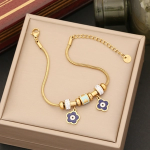 Detail eines goldenen Schlangenarmbands mit lila Blume und blauem Herz-Anhänger