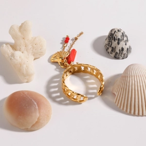 Detail of gold shell charm and red bead on hollow chain ring over coral background