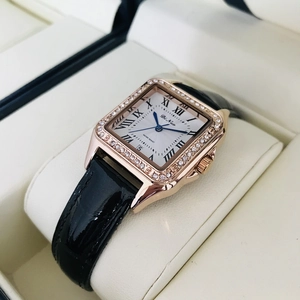 Square rose gold ladies watch with crystal bezel and black glossy leather strap on a pillow